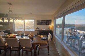 Ein Essbereich mit Tisch für vier Personen, eine Küche im Hintergrund sowie ein Blick auf eine Terrasse und die Landschaft durch große Fenster.