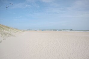 Ein Strand mit einem Steg, der ins Wasser führt, Sanddünen links und einem klaren Himmel.