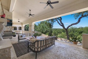 A covered outdoor seating area with a sofa, a dining table, and ceiling fans. - Blanco River estate + 2 pools + court (Wimberly)