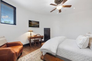 A bedroom with a bed, a desk, a chair, a window with blinds, and a ceiling fan. - Blanco River estate + 2 pools + court (Wimberly)