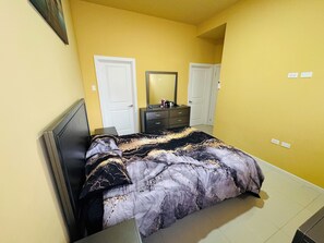 A bedroom with a bed, a dresser, a mirror, and two doors. - Hope Oasis (Kingston)
