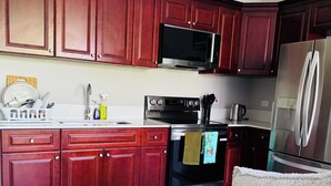 A kitchen with red cabinets, a microwave, a stove, and a refrigerator. - Hope Oasis (Kingston)