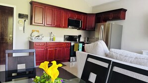 A modern kitchen with dark wood cabinets, stainless steel appliances, and a glass dining table with a vase of yellow flowers. - Hope Oasis (Kingston)