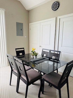 A modern dining area with a glass table, black chairs, and a potted plant. - Hope Oasis (Kingston)