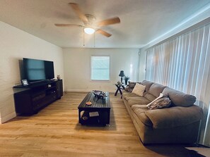A living room with a ceiling fan, a flat-screen TV on a stand, a wooden coffee table, a sofa, and a window with blinds. - Serene 3-bedroom house with AC in charming St. Petersburg (St. Petersburg)