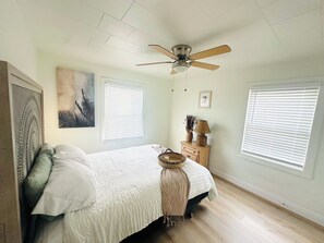 A bedroom with a bed, a ceiling fan, two windows with blinds, a nightstand with a lamp, and wall art. - Serene 3-bedroom house with AC in charming St. Petersburg (St. Petersburg)