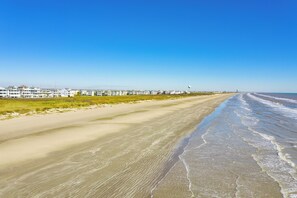 A beach with a row of white buildings, a sandy shore, and a clear blue sky. - Beach Baby Bungalow - Beachfront Condo with Gulf Views & Pointe West Amenities (Galveston)