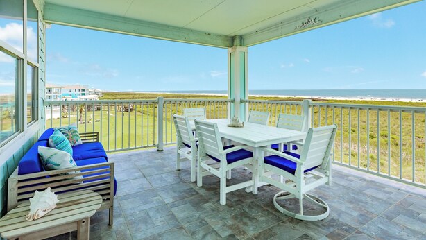 Un espace extérieur aménagé, abrité, avec une table et des chaises, un canapé avec des coussins et une vue sur la plage.