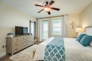 A bedroom with a bed, a television, a dresser, a ceiling fan, and a cross on the wall. - Beach Baby Bungalow - Beachfront Condo with Gulf Views & Pointe West Amenities (Galveston)