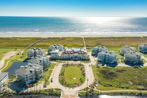 An aerial view of a coastal hotel with multiple buildings, a central courtyard, and a beach view. - Beach Baby Bungalow - Beachfront Condo with Gulf Views & Pointe West Amenities (Galveston)
