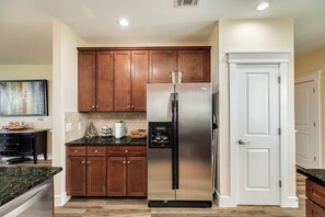 A kitchen with wooden cabinets, a stainless steel refrigerator, a coffee maker, and a white door.