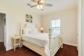 A bedroom with a bed, a nightstand, a ceiling fan, and a window. - 2nd Row Beachside Home with Easy Beach Access & Inviting Interior (Galveston)