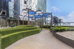 A modern outdoor area with a pathway, green landscaping, and a building with reflective glass windows. - Aerie at West Side City View and Wellness Facilities (Melbourne)