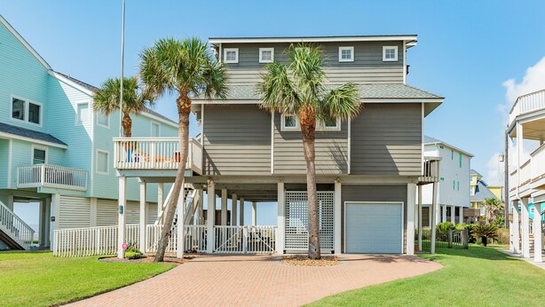 A multi-story residential building with a covered front porch, palm trees, and a brick pathway leading to the entrance. - Close to the Sand w/ Showstopping Views & Wonderful Amenities - Dog Friendly! (Galveston)