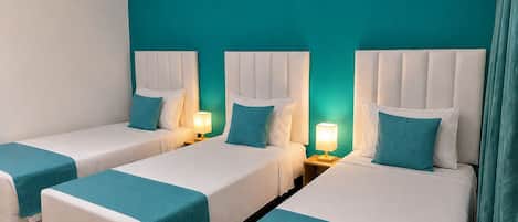 A hotel room with three beds, each with a white headboard and teal bedding. There are two wall-mounted wooden paddles above the beds.