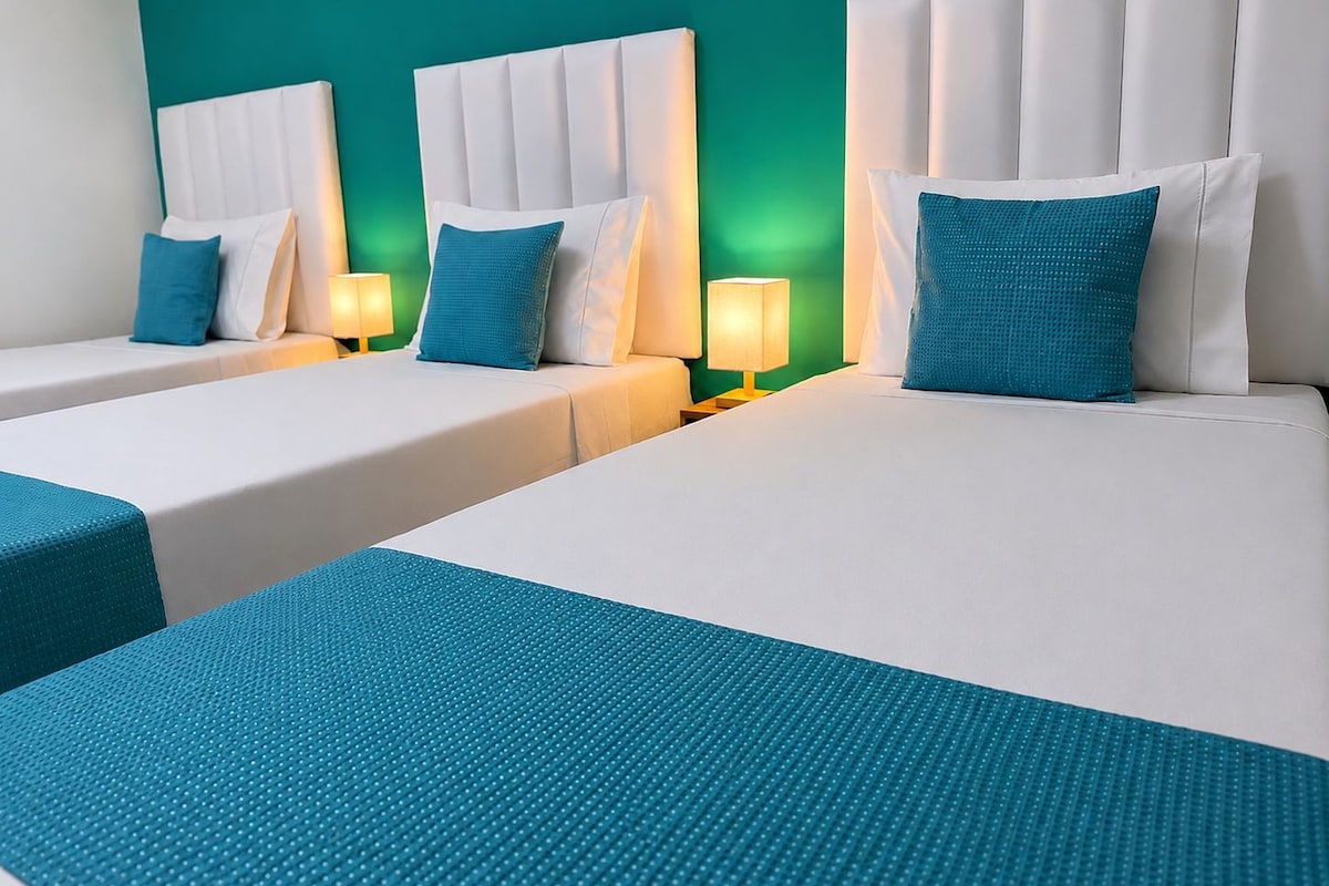 Una habitación de hotel con dos camas, cada una con cabecero blanco y almohada de color turquesa.