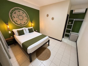 A hotel room with a bed, a green wall, a decorative wall piece, a small rug, and a kitchenette area. - Pousada Lagoas de Guarajuba (Camaçari)