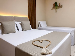 Habitación de hotel con una cama grande, dos camas más pequeñas, un estante con plantas y un adorno con forma de corazón sobre la cama.