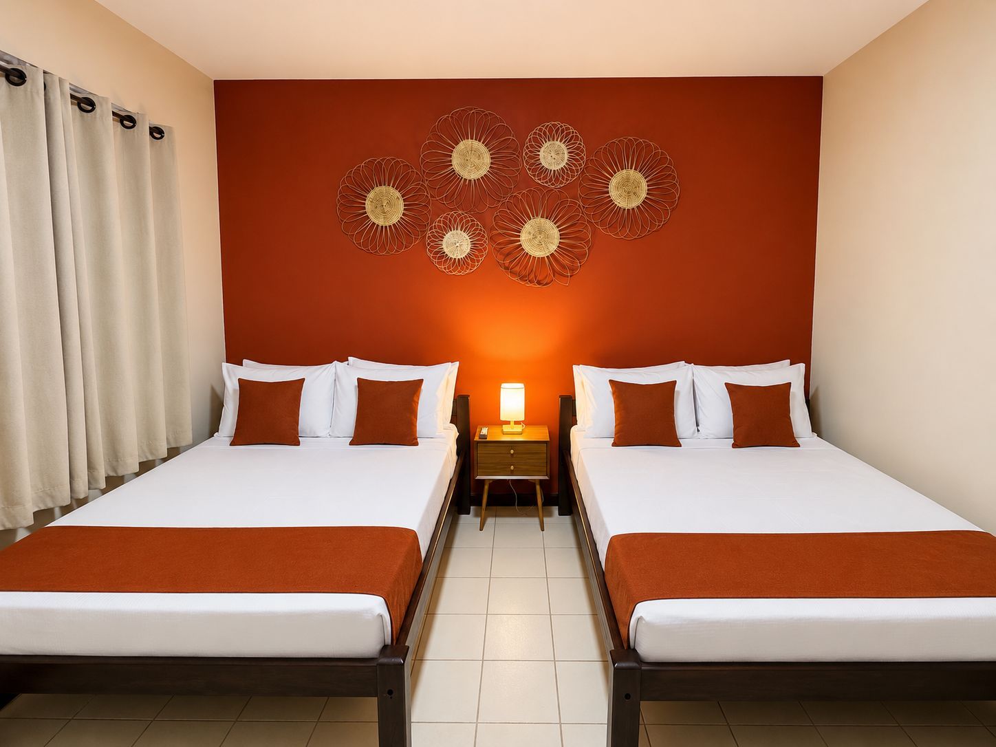 Quarto de hotel com duas camas, mesa de cabeceira, objeto decorativo na parede e cortina.