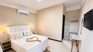 Quarto de hotel com cama, mesa de cabeceira, luminária, ar condicionado, guarda-roupa e televisão.