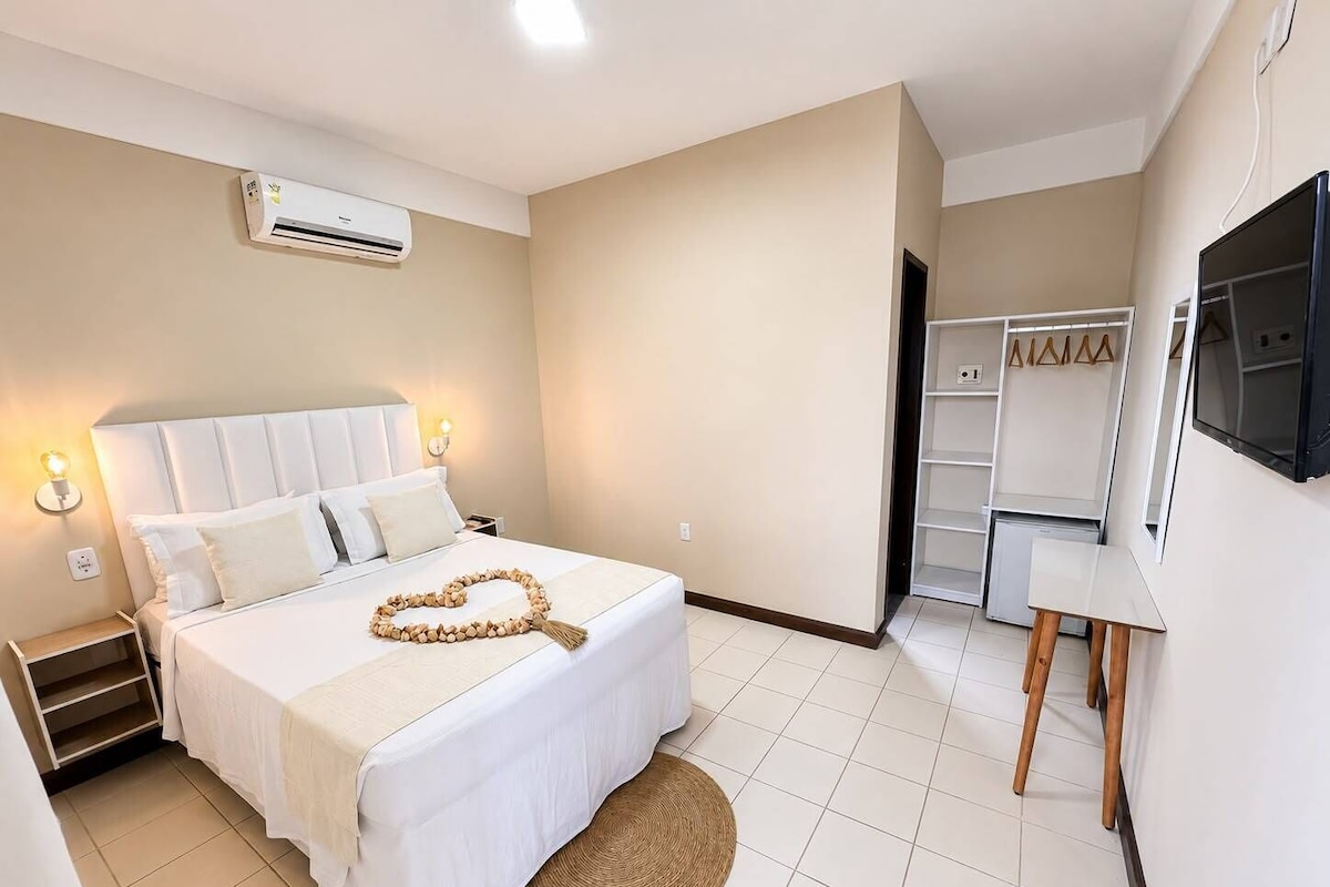 A hotel room with a bed, bedside table, lamp, air conditioning unit, wardrobe, and a television.
