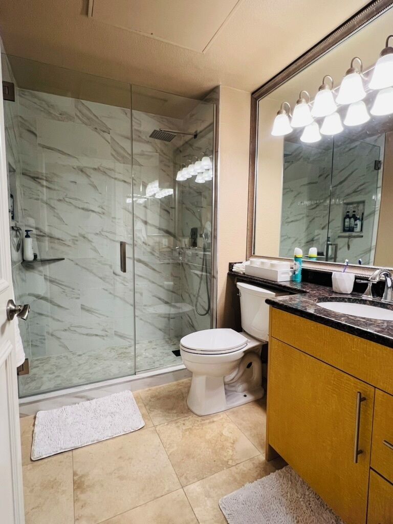 Une salle de bain avec une douche à parois de verre, des toilettes blanches, un lavabo avec un miroir et des articles de toilette posés sur le comptoir.