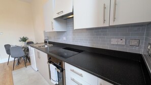 Une cuisine avec des meubles blancs, un plan de travail noir et un pare-feu en carrelage.