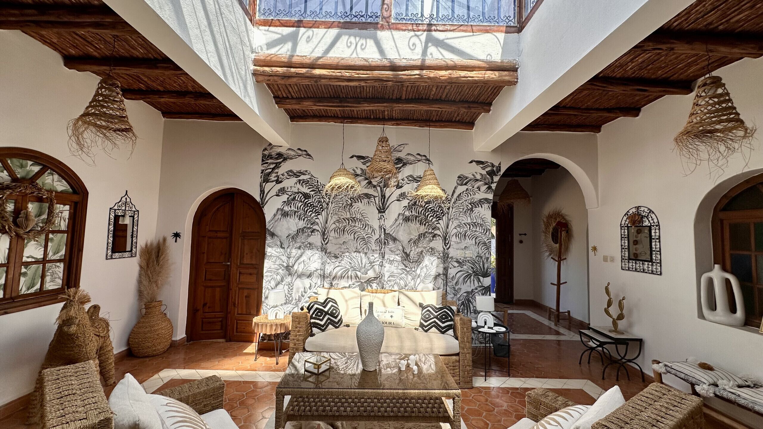 A spacious interior with a high ceiling, wooden beams, and a central seating area with a patterned rug.