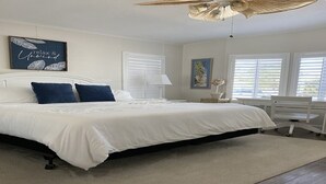 Un dormitorio con cama, paredes blancas, ventilador de techo y ventana con persianas.