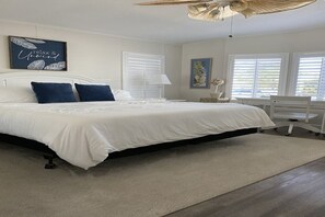 Ein Schlafzimmer mit einem Bett, weißen Wänden, einem Deckenventilator und einem Fenster mit Jalousien.