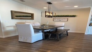 Un comedor con una mesa de madera oscura, sillas tapizadas blancas y una lámpara colgante.