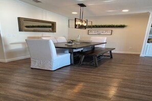 A dining area with a dark wooden table, white upholstered chairs, and a hanging light fixture.