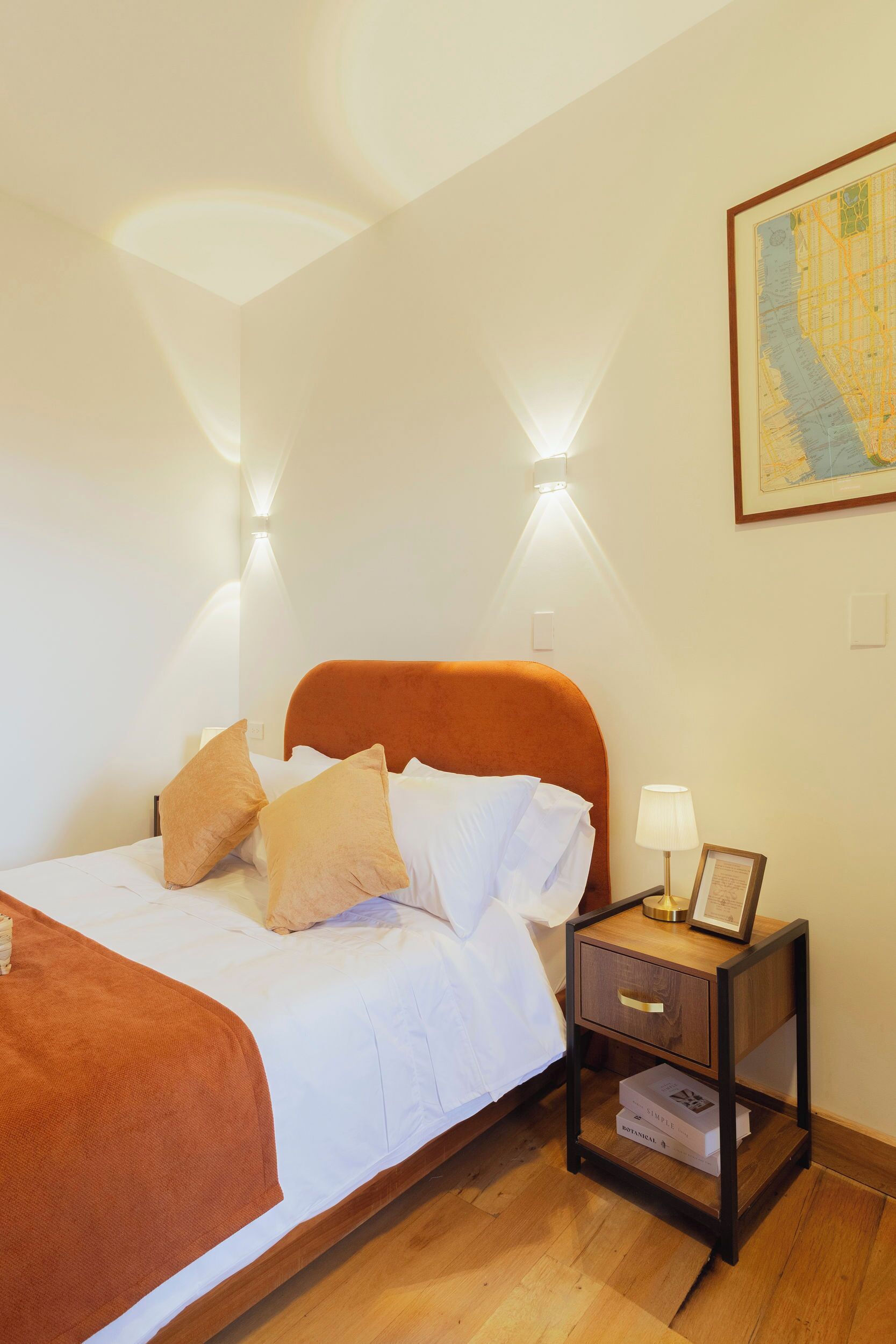 A neatly made bed with a headboard, a bedside table with a lamp, and a framed picture on the wall.