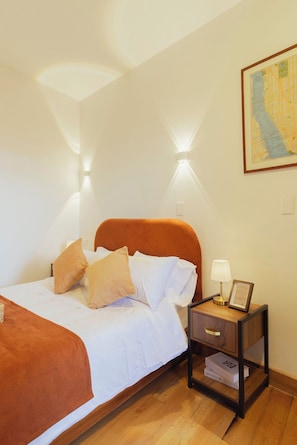 A neatly made bed with a headboard, a bedside table with a lamp, and a framed picture on the wall. - Casa Aura Hotel (Bogotá)