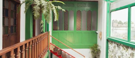 Una escalera con barandilla de madera y escalones rojos que conducen a una puerta verde con paneles decorativos.