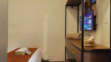 Una habitación de hotel con una cama, una mesita de noche de madera, un televisor montado en la pared y una pequeña cesta de mimbre sobre la mesita.