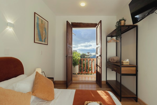 A hotel room with a bed, a desk, a TV, and a balcony with a view. - Casa Aura Hotel (Bogotá)