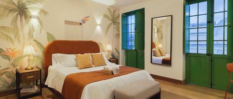 A hotel room with a bed, a nightstand, a lamp, a mirror, and a view through green doors.
