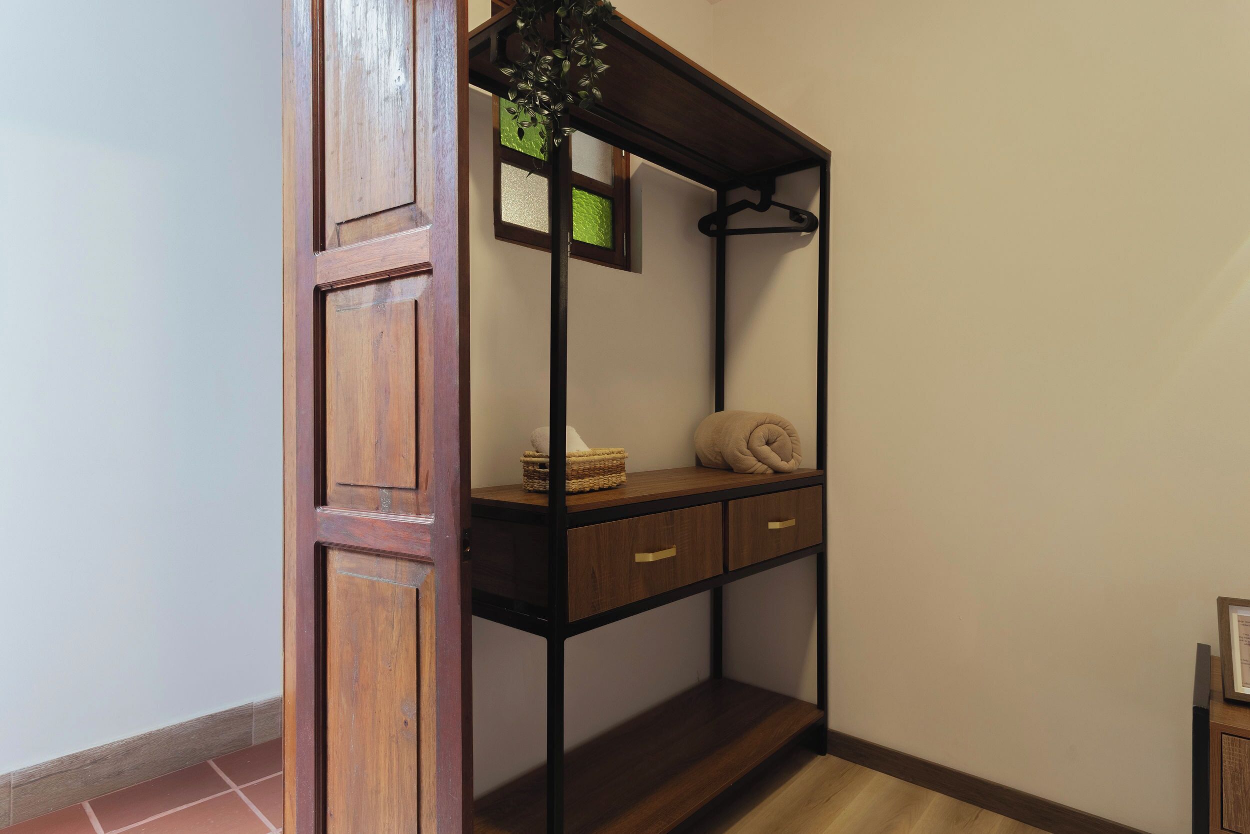 A wooden cabinet with a shelf, a hanging plant, and a rolled towel.