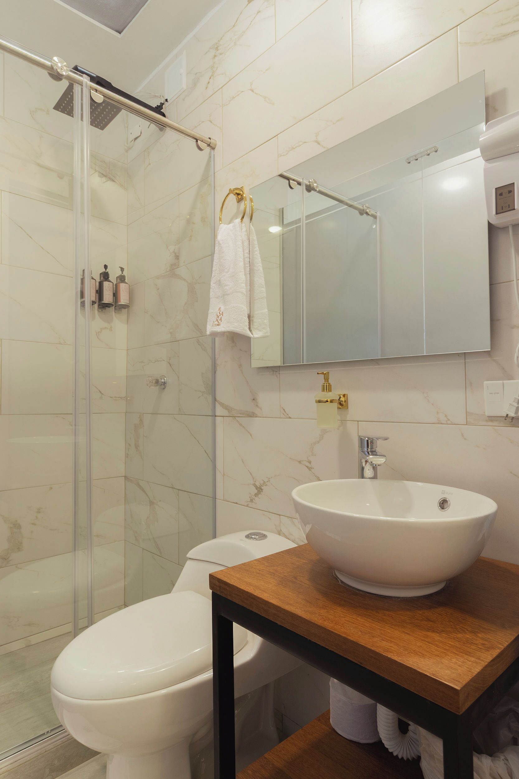 A bathroom with a glass shower enclosure, a white toilet, a sink with a marble countertop, and a mirror above the sink.