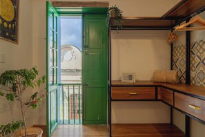 Una habitación con puerta verde, una mesita con una caja fuerte, una planta y vistas al exterior.