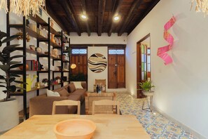 A cozy living room with a wooden table, a sofa, and a bookshelf filled with books and decorative items. - Casa Aura Hotel (Bogotá)