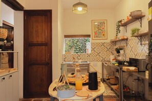 A kitchen with a wooden door, a hanging light fixture, a window with a view of greenery, and a tiled backsplash.