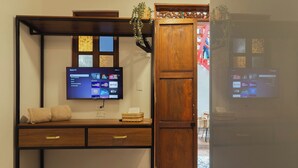 A room with a TV mounted on a wall, a wooden desk with drawers, a wicker basket, and a wooden door.