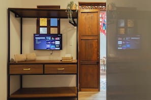 Una habitación con una televisión montada en la pared, un escritorio de madera con cajones, una cesta de mimbre y una puerta de madera.