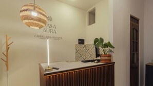 A reception desk with a modern design, a hanging light fixture, a potted plant, and a wall with a geometric pattern.