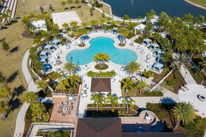 An aerial view of a resort with a central swimming pool, surrounded by lounge areas with umbrellas, palm trees, and a beach area. - House 7Q With Pool, Spa and Game Room (Kissimmee)