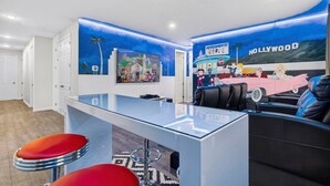 A modern interior with a bar area, seating, and a mural depicting a Hollywood theme. - House 7Q With Pool, Spa and Game Room (Kissimmee)