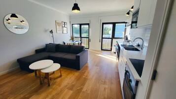 Ein modernes Wohnzimmer mit einem Ecksofa, einem runden Couchtisch und einem Essbereich mit kleinem Tisch und Stühlen.