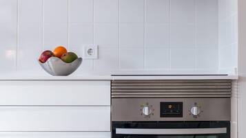 Eine Küche mit weißen Fliesen, einem Edelstahlbackofen und einer Fruchtschüssel auf der Arbeitsfläche.
